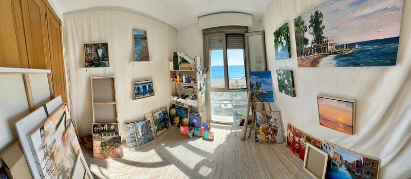 Panoramic view of Rocio Arrupe's art studio by the sea with paintings on the walls and art supplies